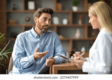 Male Patient Sharing Health Problems With Doctor Woman During Meeting In Office, Upset Sick Man Talking To Therapist Lady, Female Physician Holding Clipboard And Making Notes, Selective Focus - Powered by Shutterstock