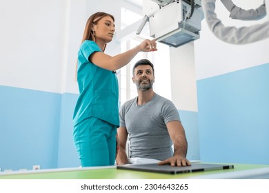 Male patient sitting while female nurse adjusting modern X-ray machine for scanning his arm or hand for injuries and fractures - Powered by Shutterstock