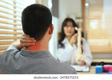 Male patient touching painful neck near explaining to physiotherapist about his pain in consulting room - Powered by Shutterstock