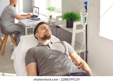Male patient undergoing intravenous vitamin therapy course treatment. Relaxed young man getting IV line medicine infusion while lying on bed at clinic or medical office - Shutterstock ID 2288199129
