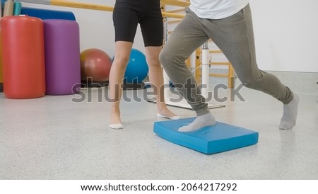 Male patients legs doing balance pad exercises with the assistance of a female therapist.