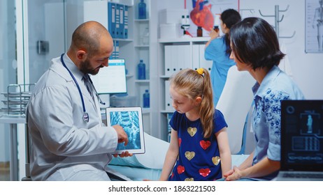 Male Pediatrician Checking Bone X-ray On Tablet In Clinic. Healthcare Practitioner Physician Specialist In Medicine Providing Health Care Service Radiographic Treatment Examination In Cabinet Hospital