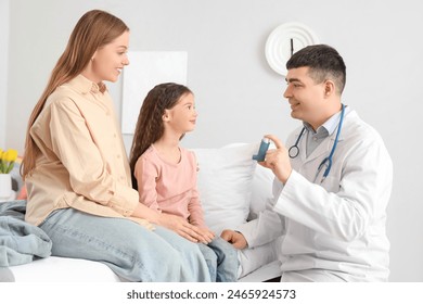 Male pediatrician showing inhaler to little girl and her mother in bedroom - Powered by Shutterstock