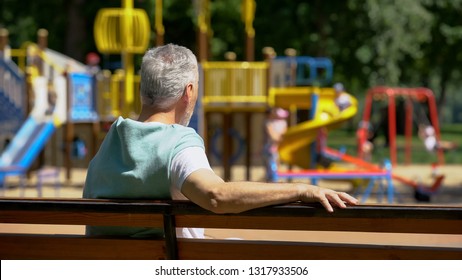 Male pensioner sitting on bench and watching grandkids on playground, family