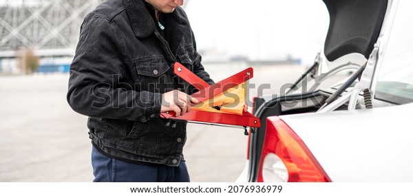 male person hold caution car accident sign and\
assemble it near the\
vehicle