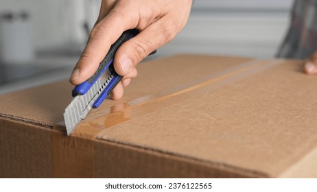 Male person hold clerical knife. Man cut mail box close up. Guy open new parcel. Hands unpacking postal package. Young adult unboxing e-commerce box. Client buy carton gift. Receiver unzip post pack.