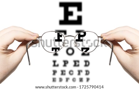 male person looking through glasses to eye examination test, letters inside the glasses are clear, others are blurred out, only hands are visible, first person point of view
