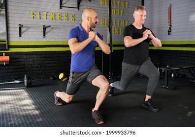 Male personal trainer motivating and supporting elderly senior man while doing forward leg lunges dynamic movement exercise in home gym small business - Powered by Shutterstock