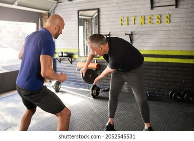 Male Personal Trainer Motivating And Supporting Elderly Senior Man While Doing Wood Choppers Dynamic Movement Exercise In Home Gym Small Business