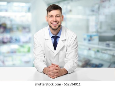 Male pharmacist near counter at work. Blurred shelves with pharmaceutical products on background - Powered by Shutterstock