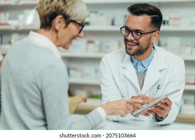 Male pharmacist selling medications at drugstore to a senior woman customer while showing her tablet - Powered by Shutterstock