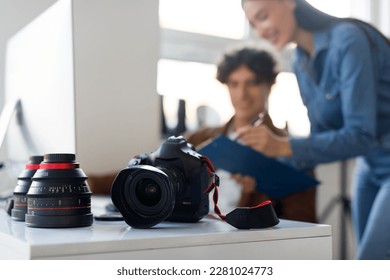 Male photographer and his assistant working together at workplace, discussing photoshoot, focus on professional photo camera and lens lying on table - Powered by Shutterstock