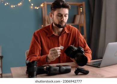 Male photographer ready to insert memory card to his professional DSLR camera while working in home office. Copy space