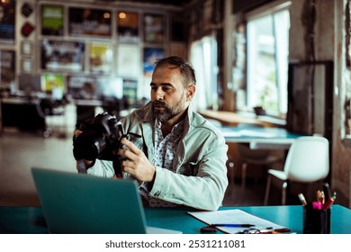 Male photographer reviewing pictures on camera while working on a laptop in creative studio - Powered by Shutterstock