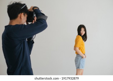 Male Photographer Take A Photo Of Teenage Model Girl In The Studio With White Background.