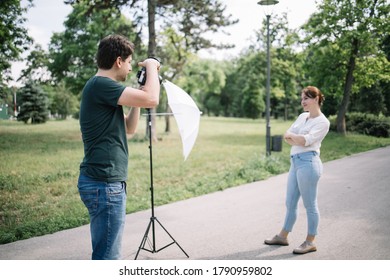 Male Photographer Taking Photos Outdoor Using Dslr Camera. Back View Of Man Taking Pictures Of Woman Who Is Posing On Park Alley.