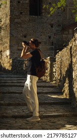 Male Photographer Taking Pictures Of Ancient City Of Mystras, Sparta. UNESCO World Heritage Archeological Sight.