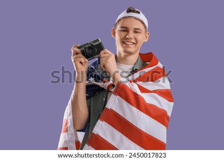 Male photographer with USA flag and photo camera on lilac background