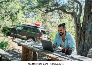 Male photographer working on a laptop outdoors in a camping. Guy freelancer, travel blogger working online at a laptop computer while hiking in the mountains outdoors. Work from anywhere in the world - Shutterstock ID 1863968218
