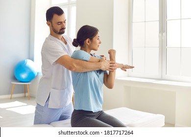 Male physiotherapist or chiropractor examining female patient's injured arm, stretching her muscles, helping her with medical exercise. Woman patient getting rehabilitation therapy in modern clinic