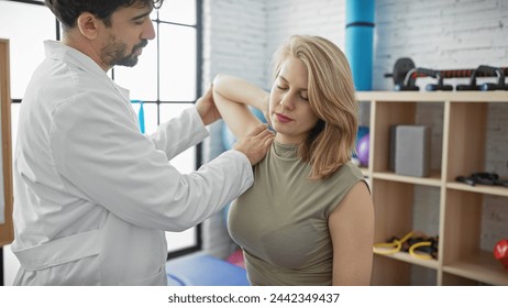 A male physiotherapist examines the arm of a female patient in a well-equipped therapy room. - Powered by Shutterstock