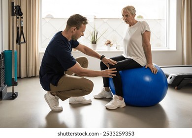 Male physiotherapist guiding elderly woman during stability ball exercise in home gym setting. Depicts personalized care, active aging, and rehabilitation for seniors in a comfortable environment. - Powered by Shutterstock