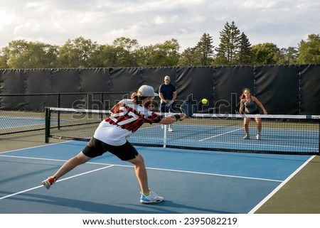 A male pickleball player returns a shot to his opponents who are approaching the net.
