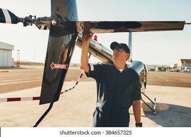 Male pilot in uniform examining helicopter tail wing. Pre flight inspection by pilot at the airport. - Powered by Shutterstock