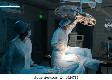 Male plastic surgeon in surgical uniforms and masks adjusting light before operation in dark operating theatre. Surgery, hospital, medical and healthcare services. Concept of surgery and emergency. - Powered by Shutterstock