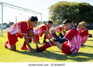 Male players holding legs of multiracial teammates practicing crunches on grassy field at playground. Assisting, unaltered, soccer, sport, teamwork, competition, exercising, training and fitness. - Powered by Shutterstock