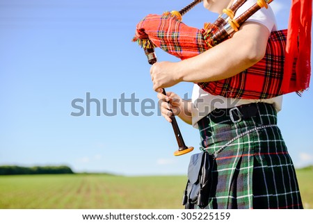 Male playing Scottish traditional pipes on green summer outdoors background, closeup image 