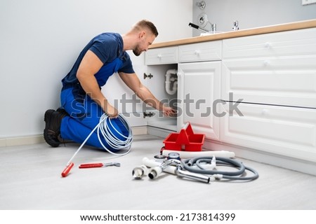 Male Plumber Cleaning Clogged Sink Pipe In Kitchen