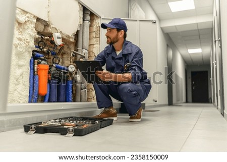 Male plumber diagnoses pipes in water supply system before repairing and makes notes in clipboard
