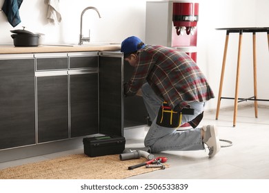 Male plumber fixing sink in kitchen