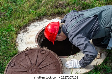 A male plumber opened the hatch of a water well and looks inside. Inspection of water pipes and meters. - Shutterstock ID 2227107101