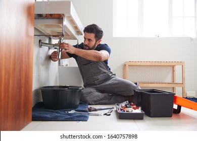 Male Plumber Working To Fix Leaking Sink In Home Bathroom
