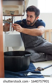 Male Plumber Working To Fix Leaking Sink In Home Bathroom