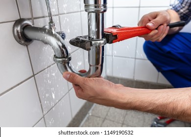 Male Plumber's Hand Repairing Sink Pipe Leakage With Adjustable Wrench