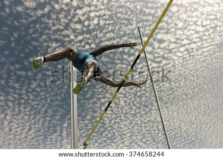 Male pole vaulter jumps  over the yellow black striped bar