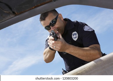 Male police officer aiming gun at broken car