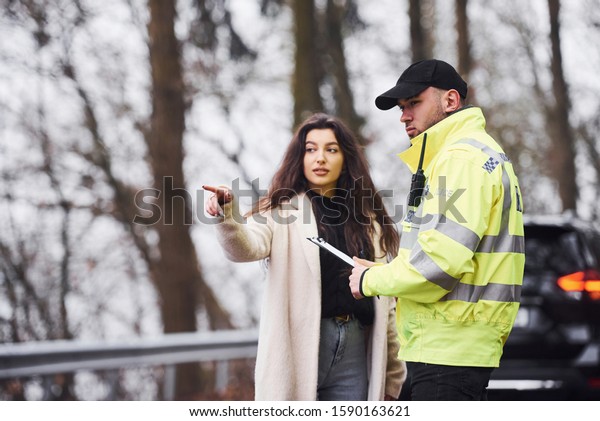 Male police officer in green uniform\
talking with female owner of the car on the\
road.