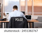 Male police officer working in office, back view