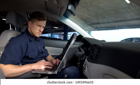 Male Police Officer Working On Laptop In Car, Filling Data In Crime Report