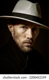 Male Portrait. Art Portrait Of A Calm Mature Man With Beard And Moustache Dressed In Black Coat And A Hat. Dark Key Portrait On A Black Background.  Male Beauty.