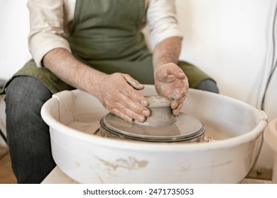 A male potter carefully sculpts a clay bowl with the help of a potter's wheel in a studio setting. - Powered by Shutterstock