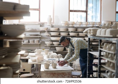 Male potter writing the orders in notebook at workshop - Powered by Shutterstock