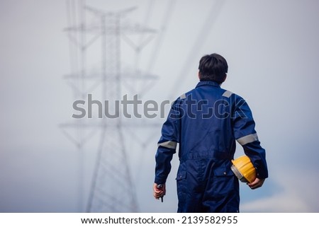 A male power engineer in a yellow helmet inspects the power line under a high voltage electrical line.