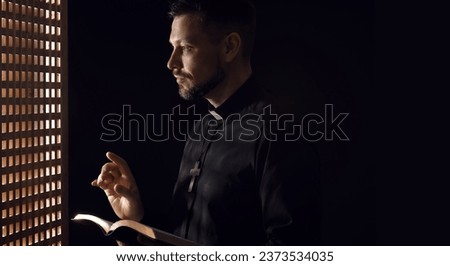 Male priest with Bible in confession booth