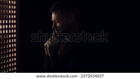 Male priest with cross in confession booth