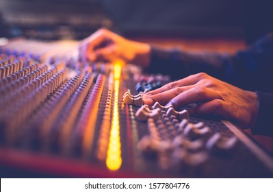 male producer, sound engineer hands working on audio mixing console in broadcasting, recording studio